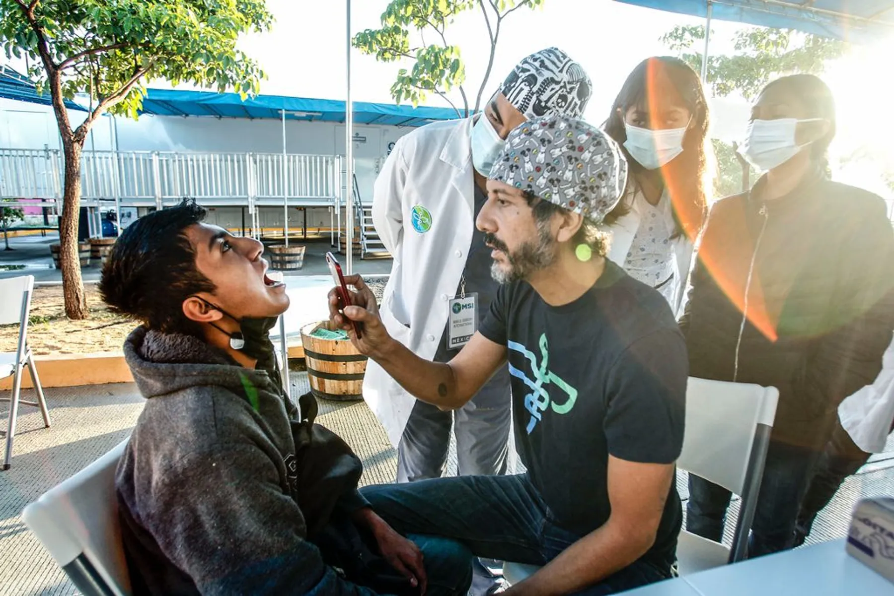 Dr. Nico Sierra explora la boca de un paciente joven con una linterna en una consulta al aire libre