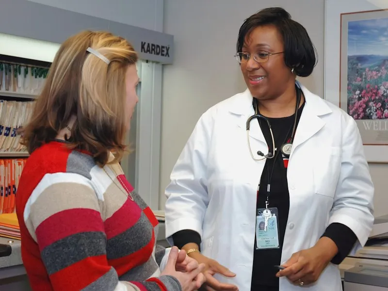 Médica con bata blanca conversando con una paciente en una consulta