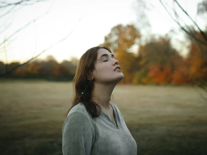 Mujer joven respirando con calma y los ojos cerrados en un campo en otoño
